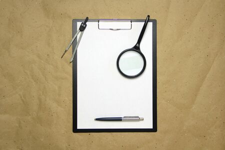 A tablet with a white sheet of A4 format with magnifier, pen and divider on a beige craft paper. Concept of analysis, study, attentive work. Stock photo with empty place for your text and design.の写真素材