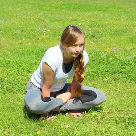 Young woman of European appearance does yoga in summer nature. Woman sitting in cockerel pose, kukkutasana. High quality photo for web and print with empty space for text and design.の写真素材