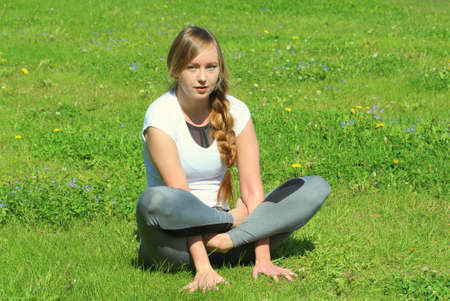 Young woman of European appearance does yoga in summer nature. Woman sitting in cockerel pose, kukkutasana. High quality photo for web and print with empty space for text and design.の写真素材