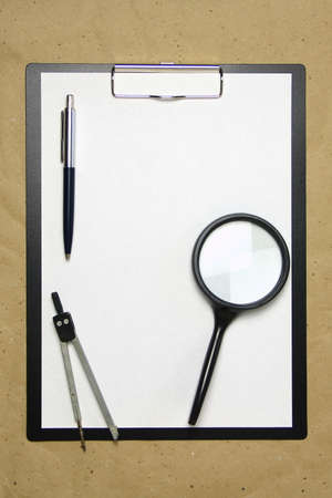 A tablet with a white sheet of A4 format with magnifier, pen and divider on a beige craft paper. Concept of analysis, study, attentive work. Stock photo with empty place for your text and design.の写真素材