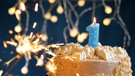 Birthday cake with 1 number candles and burning sparkler on blue backgraund. Close-up view
