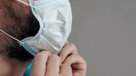 Attractive man surgeon doctor puts surgical mask on his face. Preparation for surgery, infection...