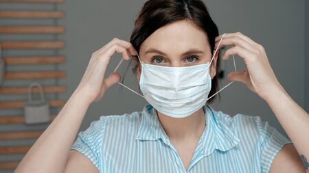 Attractive girl puts on surgical mask on her face. Cold, flu, virus, acute respiratory infections, quarantine, epidemic, irony, sarcasm concept. Close up viewの写真素材