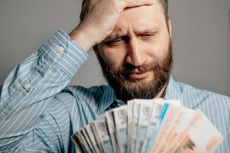 Russian ruble falling inflation concept. Portrait of man looks at bundle of money rubles holding his...