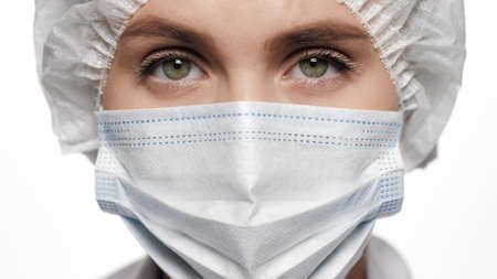 Close-up of concentrated woman doctor in surgical mask is looking at camera. Operation, medical...