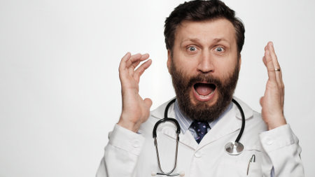Doctor is scared, terrified. Frightened man doctor on white background looking at camera throws his hands up and screams, he is very scared and just terrifiedの写真素材