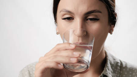Woman is drinking water. Woman on white background drinks water from glass. Close-up