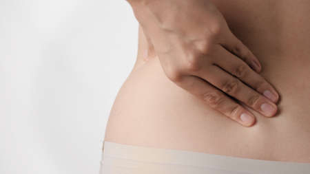 Backache. Female hand touches and presses on lower back on white background. Close-up