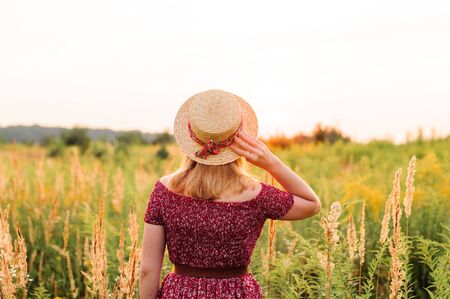 Beautiful girl in red dress in yellow walking through field, sunset time. golden hour. village sceneryの写真素材