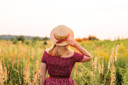 Beautiful girl in red dress in yellow walking through field, sunset time. golden hour. village sceneryの写真素材