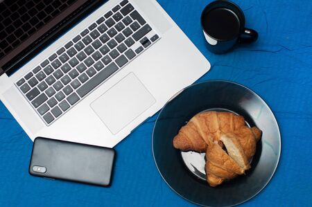 Typical blogger morning. Laptop and smartphone on the bed. Croissants with tasty coffeeの写真素材