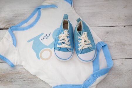  shoes for the baby and clothing for a boy on a white wooden background. top viewの写真素材