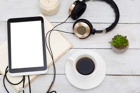 Cozy home still life. Tablet, cup and golden headphones on a white wooden backgroundの写真素材