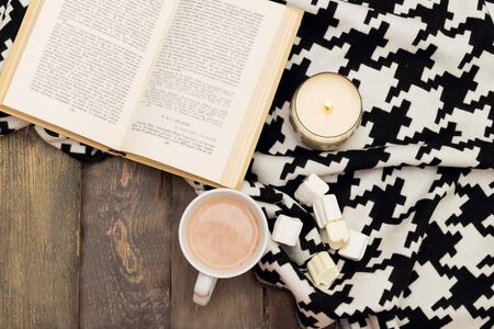 Hot chocolate, marshmallow, open book and candle on a wooden background. View from aboveの写真素材