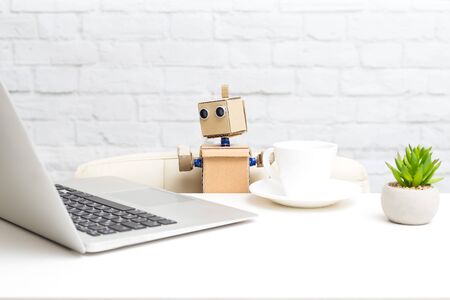 The robot works behind a laptop and drinks coffee. Artificial Intelligenceの写真素材