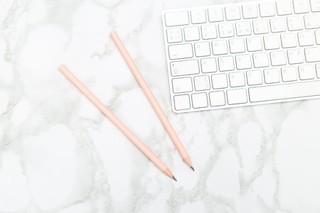 White keyboard and pink pencils on a marble background. Flat lay