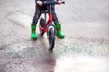 Balance bike and Green rubber boots and a puddle. Childhood