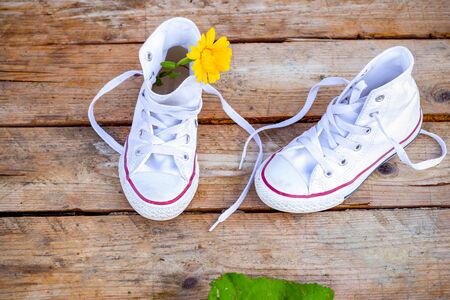 White sneakers with a yellow flower on a wooden background. Flat layの写真素材