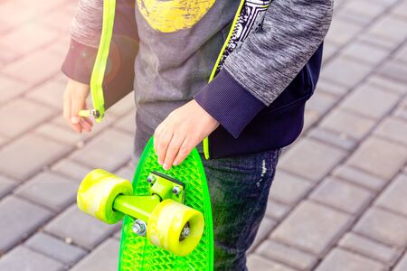 The boy holds in his hand a green skateboard. Childhood