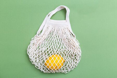 Mesh shopping bag with lemons on green canvas background. reusable concept. BACK TO NATUREの写真素材