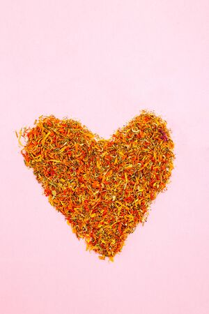 Dried calendula in the shape of a heart on a pink background. Verticalの写真素材
