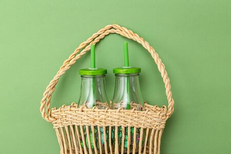 Glass bottle in wicker basket on green background. Sustainable lifestyle. Undertoneの写真素材