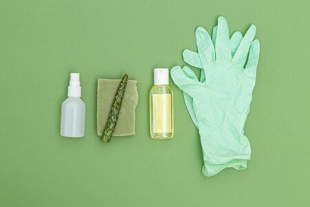 Antiseptic, rubber gloves and aloe vera lea fon green background. Flat lay. Undertone