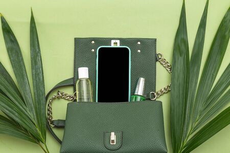 Handbag, phone, nail polish and natural leaves on green background. Monochrome. Flat layの写真素材