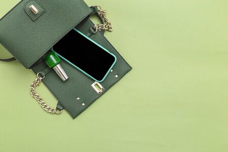 Handbag, phone, nail polish on green background. Monochrome. Minimal. Copy spaceの写真素材