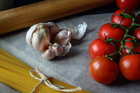 Food background. Flat lay of fresh tomatoes, pasta and garlic on baking paper. Top viewの写真素材