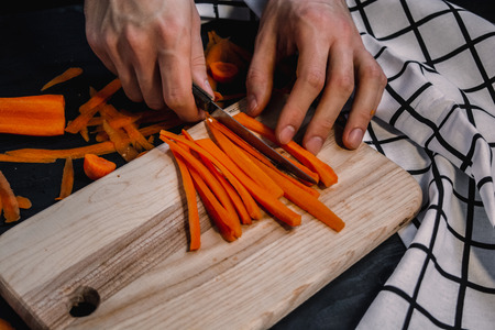 Cutting carrot on a wooden board for meal preparationの写真素材