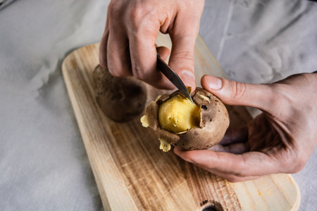 Fresh hot boiled potato with peeled skins. Hand holding ready to cook or eat, on table. Concept and...