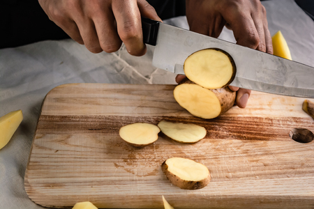 Chef's hand cutting fresh and delicious potatoes for cooking on a table. Healthy food.の写真素材