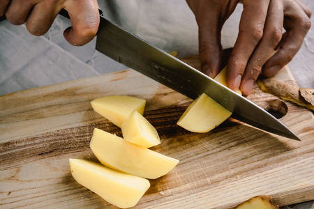 Chef's hand cutting fresh and delicious potatoes for cooking on a table. Healthy food.の写真素材