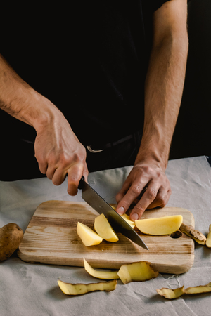 Chef's hand cutting fresh and delicious potatoes for cooking on a table. Healthy food.の写真素材