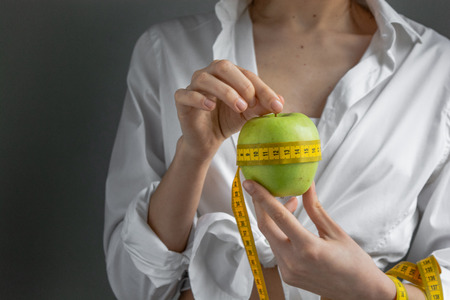 Young pretty woman holding apple and measure tapeの写真素材