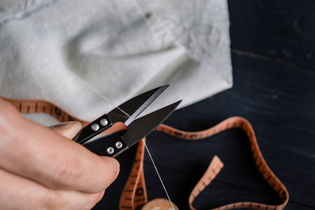 Tailor cutting a thread with scissors, close up, black background