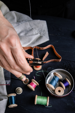 Tailor cutting a thread with scissors, close up, black background