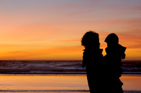 Daughter in her mother's arms and mom herself are silhouetted against the gorgeous sunset at Pacific ocean in San Francisco.の写真素材