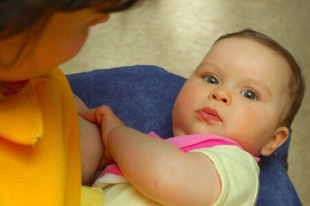 Baby girl looks up from breastfeeding, clasping mother's breast tightly.