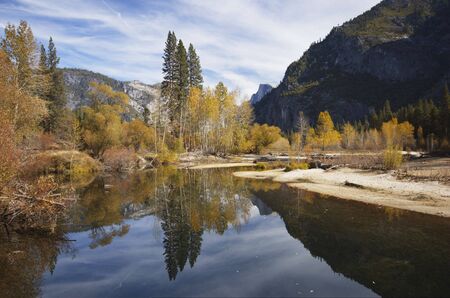 Half Dome is reflected in the calm waters of Merced River amid bright fall colors in Yosemite Valley, Sierra Nevada, California.の写真素材