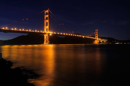 Golden Gate Bridge as seen from Fort Point overlook is glowing in the night with star trails in the...