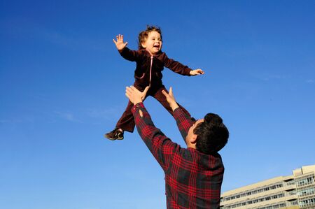 A happy two year old girl tossed into the blue sky by her father.の写真素材