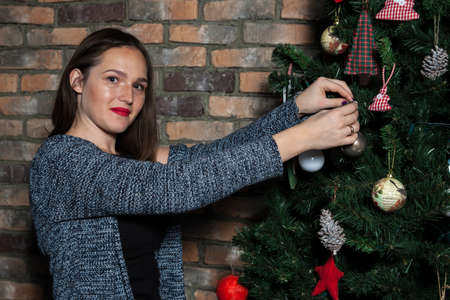 beautiful girl with red lips hangs a ball on the christmas treeの写真素材