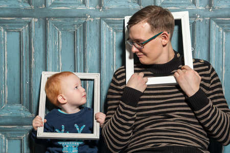 Photo of a little redhead boy and dad in looking at each other and holding a wooden frame in their hands, on a vintage backgroundの写真素材