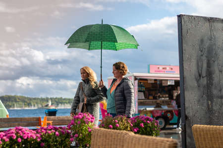 Oslo.Oslo/Norway-09.17.2020: Rainy day in Oslo, Aker Brygge. People walking with umbrella.のeditorial素材