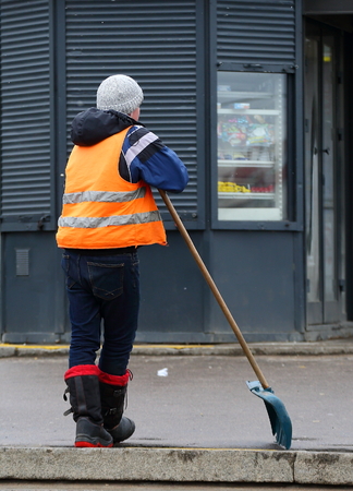 Janitor in an orange vest is leaning on a shovelの写真素材