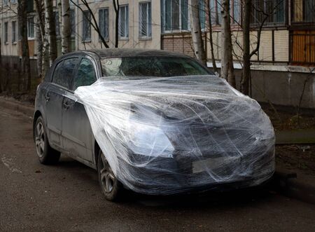 A wrecked car wrapped in plastic wrap in the yard of a houseの写真素材