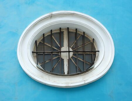 An oval barred window in a blue wallの写真素材