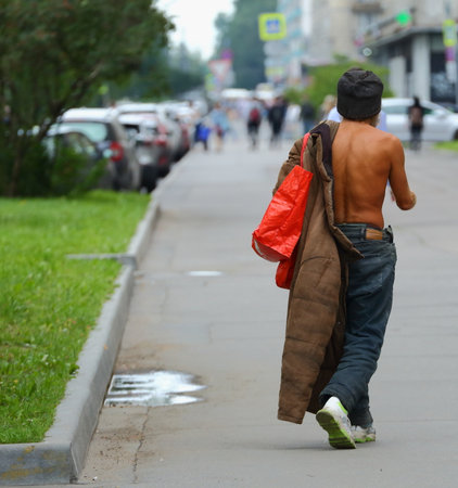 Naked to the waist a tanned tramp with a coat over one shoulder, prospekt Bolshevikov, Saint Petersburg, Russia August 2020のeditorial素材